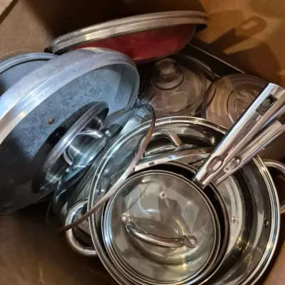 Sale Photo Thumbnail #69: Cardboard box filled with assorted stainless steel pots, pans, and matching glass and metal lids.
