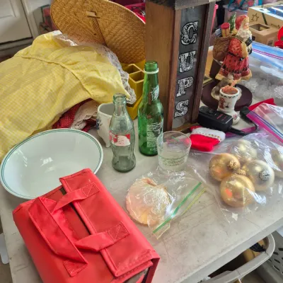 Sale Photo Thumbnail #27: Assorted household goods, including vintage glass bottles, a wooden cup dispenser, Christmas ornaments, and a red lunch tote.