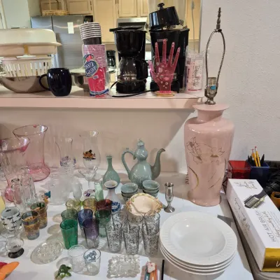 Sale Photo Thumbnail #13: A tabletop arrangement featuring vintage glassware, a pink ceramic lamp base, a celadon tea set, stacked dinnerware, and various small household collectibles.