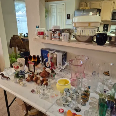Sale Photo Thumbnail #15: Folding tables filled with assorted household glassware, ceramic vases, novelty mugs, and kitchen items for sale.