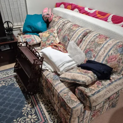 Sale Photo Thumbnail #42: Vintage floral stripe upholstered sofa filled with throw pillows, linens, and paired with a small dark wood carved shelf.