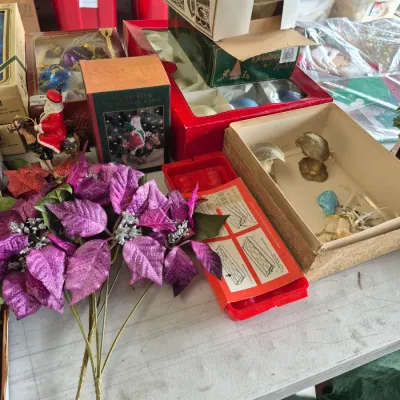 Sale Photo Thumbnail #39: Collection of vintage Christmas decorations, including boxed glass ornaments, a Santa's From Around the World figurine, artificial purple poinsettias, and novelty items.