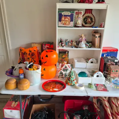 Sale Photo Thumbnail #21: Collection of seasonal holiday decor on display, featuring plastic jack-o'-lantern buckets, Christmas village houses, a nutcracker, and string lights.