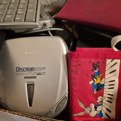 Sale Photo Thumbnail #54: Vintage Sony Discman ESP2 portable CD player model D-E401, displayed alongside a Looney Tunes graphic wallet and a computer keypad.
