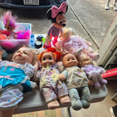 Collection of vintage baby dolls, troll dolls, and a large Minnie Mouse figure displayed on a folding table at a garage sale.