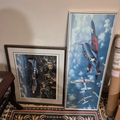 Sale Photo Thumbnail #46: Pair of framed aviation art prints depicting WWII-era military aircraft in flight, presented in silver and brown frames.