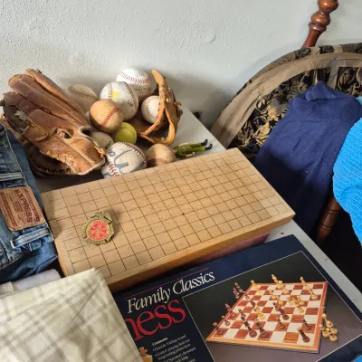 Sale Photo Thumbnail #35: Collection of vintage items including worn leather baseball gloves and balls, a wooden grid game board, a Family Classics Chess game in box, and denim jeans.