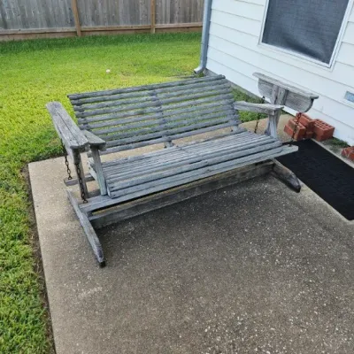 Weathered wooden porch glider bench with slatted seat and back rest, showing heavy finish wear and patina.