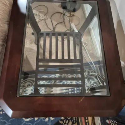 Sale Photo Thumbnail #43: Dark wood end table featuring a glass insert top and a slatted lower shelf, showing minor surface wear.