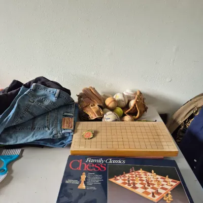 Sale Photo Thumbnail #29: Collection of tabletop games and sports memorabilia, including a Pressman Family Classics chess game in its original box, a wooden Go board, vintage baseball gloves, assorted baseballs, and folded denim jeans.