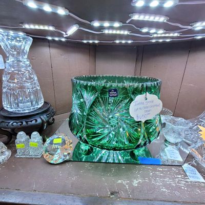 Irena green emerald cut-to-clear crystal bowl displayed alongside other clear crystal decorative objects on a glass shelf.