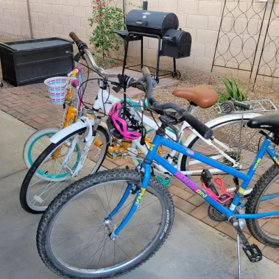 Collection of outdoor items including a blue KHS Montana Crest mountain bike, a white cruiser bicycle, a child's yellow bike with a...
