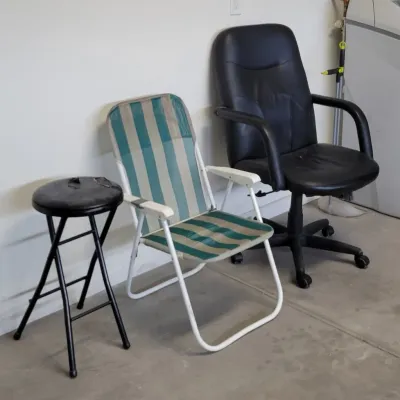 Collection of seating including a black folding stool with a damaged seat, a blue and tan striped folding lawn chair, and a black faux...