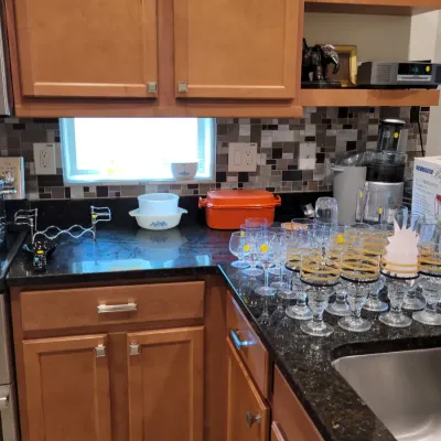 Kitchen counter displaying assorted glassware with gold rims, a bright orange Le Creuset-style roasting pan, and Pyrex casserole dishes.