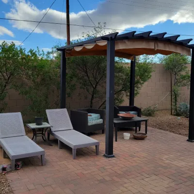 Outdoor patio set featuring a freestanding dark metal pergola with a retractable beige canopy shade, accompanied by light gray lounge...