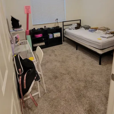 Bedroom featuring a modern black metal platform bed frame, a small desk with a white chair, and a black low shelving unit with various...
