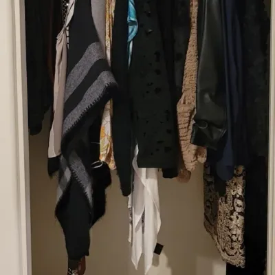 Closet filled with women's hanging clothing, including sweaters, jackets, ponchos, and formal attire.