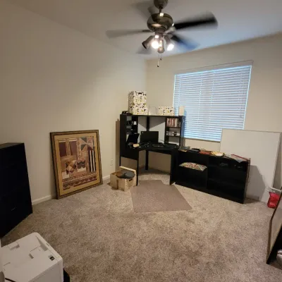 Home office space featuring a black corner desk with hutch, matching storage shelf, framed abstract art, and office supplies.