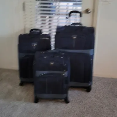 Three-piece set of matching dark blue and grey softside rolling luggage, including various sizes with telescoping handles.
