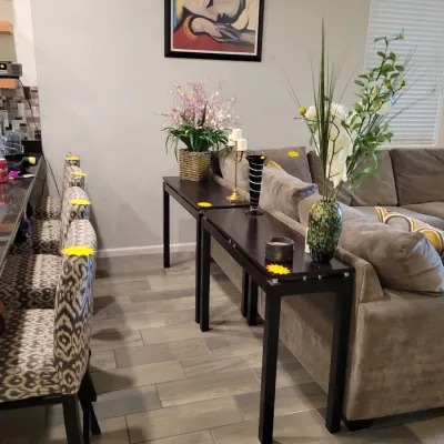 Contemporary dark wood sofa console tables displayed behind a taupe sectional couch, alongside pattern-upholstered bar stools and home...