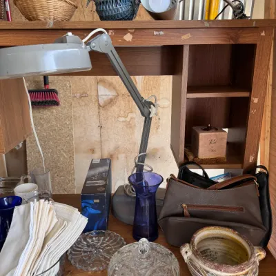 Sale Photo Thumbnail #12: Vintage Luxo-style swing arm drafting desk lamp displayed on a wooden desk alongside glassware, linens, a purple glass vase, handbags, and a ceramic planter. Category: Home Decor > Lighting & Home Accessories.