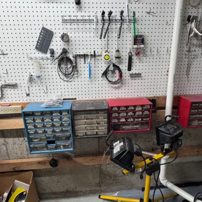Sale Photo Thumbnail #53: Workshop organizer setup featuring Akro-Mils multi-drawer parts cabinets, a yellow tripod dual halogen work light, and assorted hand tools mounted on a white pegboard wall.