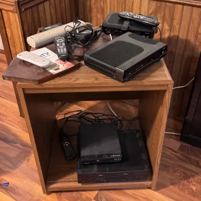 Sale Photo Thumbnail #61: Collection of home media electronics on a wooden corner stand, including Motorola cable boxes, a DVD player, VCR, power strip, and various remote controls.