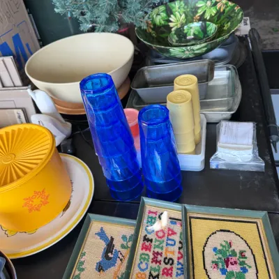 Sale Photo Thumbnail #15: Assortment of vintage housewares including stacked cobalt blue and yellow Tupperware plastic tumblers, a yellow Tupperware Servalier canister, framed needlepoint art, baking pans, ceramic bowls, and floral salad bowls.
