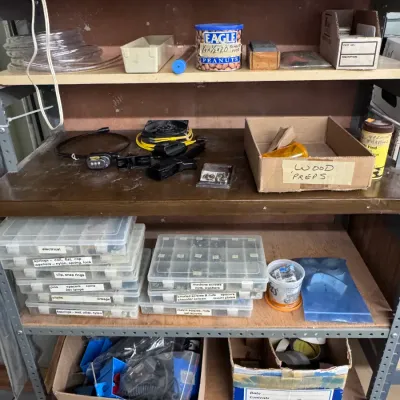 Sale Photo Thumbnail #49: Metal workshop utility shelving unit loaded with hardware, clear compartment organizers, fasteners, an Eagle Peanuts tin, and various workshop supplies.