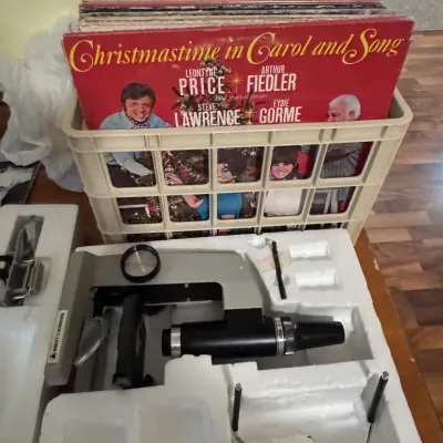 Sale Photo Thumbnail #44: Bausch & Lomb vintage microscope in original Styrofoam packaging casing, positioned next to a crate filled with classic vinyl LP records including 'Christmastime in Carol and Song'.