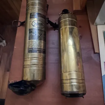 Sale Photo Thumbnail #43: Vintage Pyrene brass hand-pump fire extinguisher set made in Newark, New Jersey, USA. These antique brass polished cylinders feature original Pyrene Manufacturing Company metal instruction plates, mounting brackets, and T-handle pumps, showing a rich pati