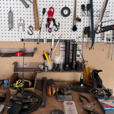 Sale Photo Thumbnail #4: Assorted workshop tools and hardware organizing setup featuring a white pegboard loaded with hand saws, a claw hammer, screwdrivers, flashlights, and a Radio Shack CB radio station with a thermometer on the workbench.