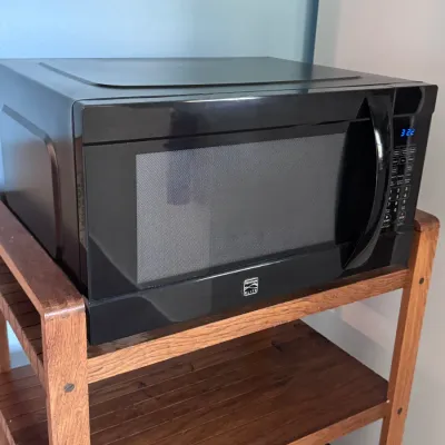 Sale Photo Thumbnail #18: Kenmore Elite countertop microwave oven in a black finish, featuring a digital keypad display and handle, resting on a multi-tier slatted wooden utility cart.