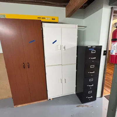 Sale Photo Thumbnail #59: Office storage units including a brown wood laminate two-door cabinet, a white four-door storage cabinet, and a black metal four-drawer vertical filing cabinet.