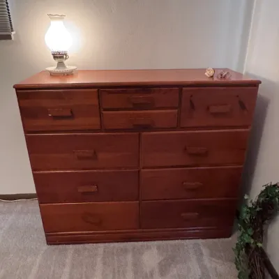 Sale Photo Thumbnail #30: Vintage solid pine wooden dresser with an eight-drawer configuration and matching wooden pulls, styled with a small illuminated accent lamp on top.