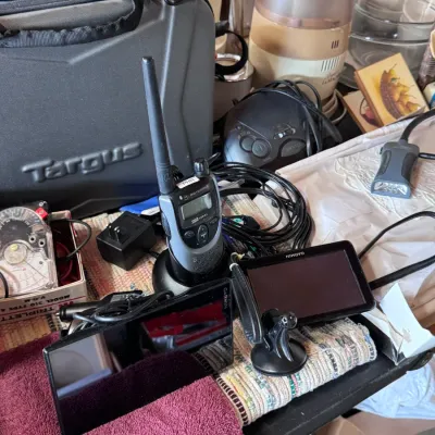Sale Photo Thumbnail #2: Electronics assortment featuring a Motorola two-way radio in charging dock, Garmin GPS units, a Targus carrying case, and vintage Triplett Model 310 V-O-M meter.