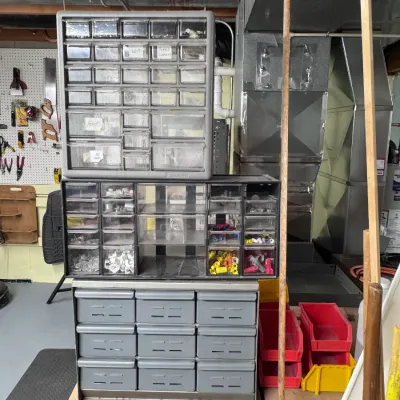 Sale Photo Thumbnail #46: A stack of Akro-Mils plastic multi-drawer parts cabinets filled with various hardware and electrical connectors, displayed in a workshop environment.