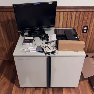 Sale Photo Thumbnail #37: eMachines computer monitor resting on a grey metal rolling storage cabinet, alongside computer accessories including an ASUS USB-BT500 Bluetooth adapter, cables, and various small electronics.