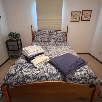 Sale Photo Thumbnail #24: Title: Wooden Four-Poster Bed Frame with Paisley Bedding and Folded Linens. Category: Furniture > Beds & Bed Frames. Traditional style wooden bed frame featuring four low corner posts and a arched footboard, dressed in a blue and white paisley comforter s