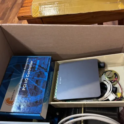 Sale Photo Thumbnail #38: Box of mixed vintage electronics and computer parts, including a Logitech device, a boxed PCI I/O Controller add-on card, various connecting cables, and small hardware components.
