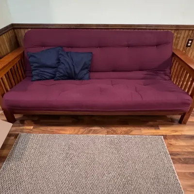 Sale Photo Thumbnail #40: Mission-style convertible wooden futon sofa featuring slatted sides, a deep purple tufted mattress cushion, and two blue accent pillows. Title: Mission Style Convertible Futon Sofa. Categories: Furniture > Sofa Beds & Futons.