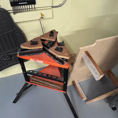 Sale Photo Thumbnail #50: Title: Vintage Triangular Clamping Workbench Stand | Category: Tools & Workshop Equipment. Triangular portable clamping workstation featuring a metal tripod frame, orange shelf base, adjustable wooden top jaws with bench dogs, and hand-crank mechanism.
