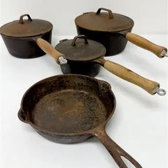 Sale Photo Thumbnail #43: Set of four vintage cast iron cookware pieces, including three saucepans with wooden handles and matching lids, and a open skillet, showing surface rust and patina.