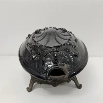 Sale Photo Thumbnail #52: Victorian-style ornate black cast iron pot belly stove top or heater, featuring intricate scrolled detailing and raised footed base.
