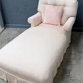 Sale Photo Thumbnail #66: Blush pink upholstered chaise lounge featuring a tufted backrest, rolled arms, matching accent pillow, and a pleated skirt base.