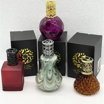 Sale Photo Thumbnail #49: Collection of four La-Tee-Da fragrance lamp bottles in assorted colored glass and decorative pierced metal tops, accompanied by three original black boxes.