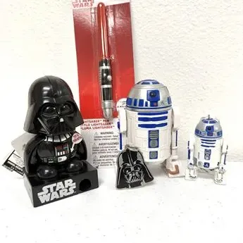 Sale Photo Thumbnail #60: Collection of Star Wars merchandise, featuring a Darth Vader desk accessory, an R2-D2 figure, a Darth Vader keychain, and a novel lightsaber pen in original packaging.