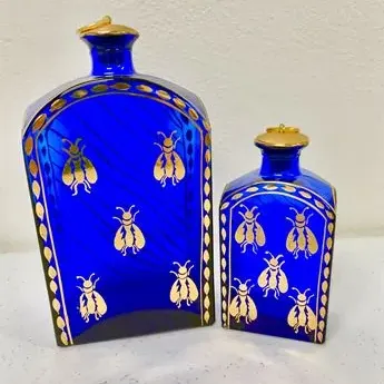 Sale Photo Thumbnail #22: Pair of cobalt blue glass decanters featuring gilded bee motifs and gold-trimmed stoppers.
