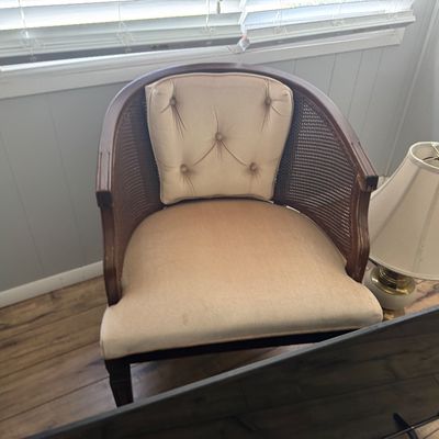 Vintage barrel-back arm chair featuring a dark wood frame with cane webbing sides, a tufted cream upholstered backrest, and a matching...