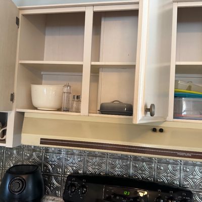 Open white kitchen upper cabinets containing cookware, salt and pepper shakers, and plastic storage containers, positioned above a...